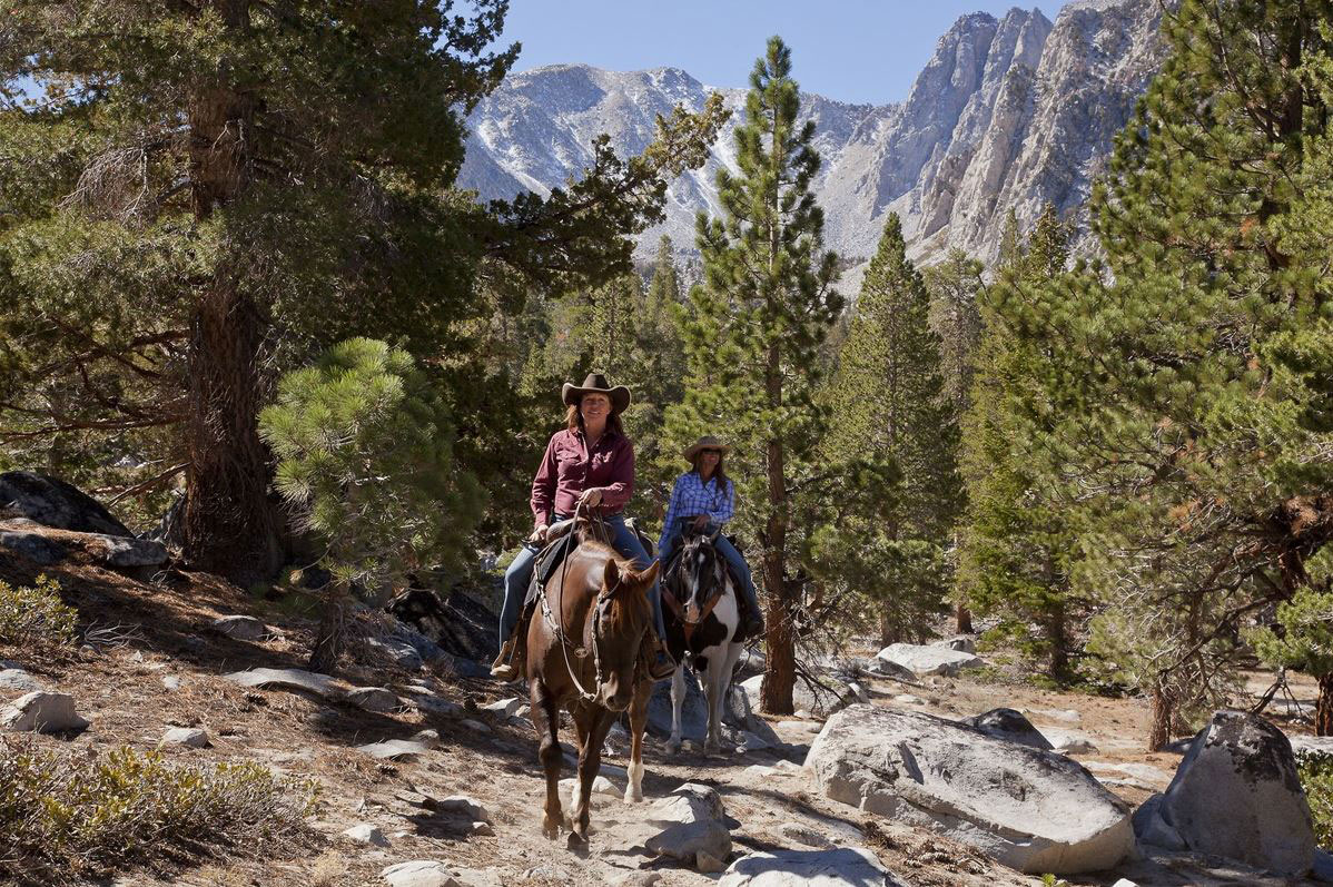 Two women horseback riding on trail